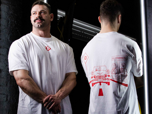 A person wearing a white unisex muscle fit t-shirt with a unique Pitstop-inspired graphic, standing in front of a mirror.