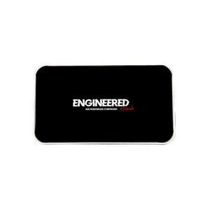 A black bod scale device with rounded corners sits on a wooden surface. The front displays the white and red 'ENGINEERED MUSCLE' logo.